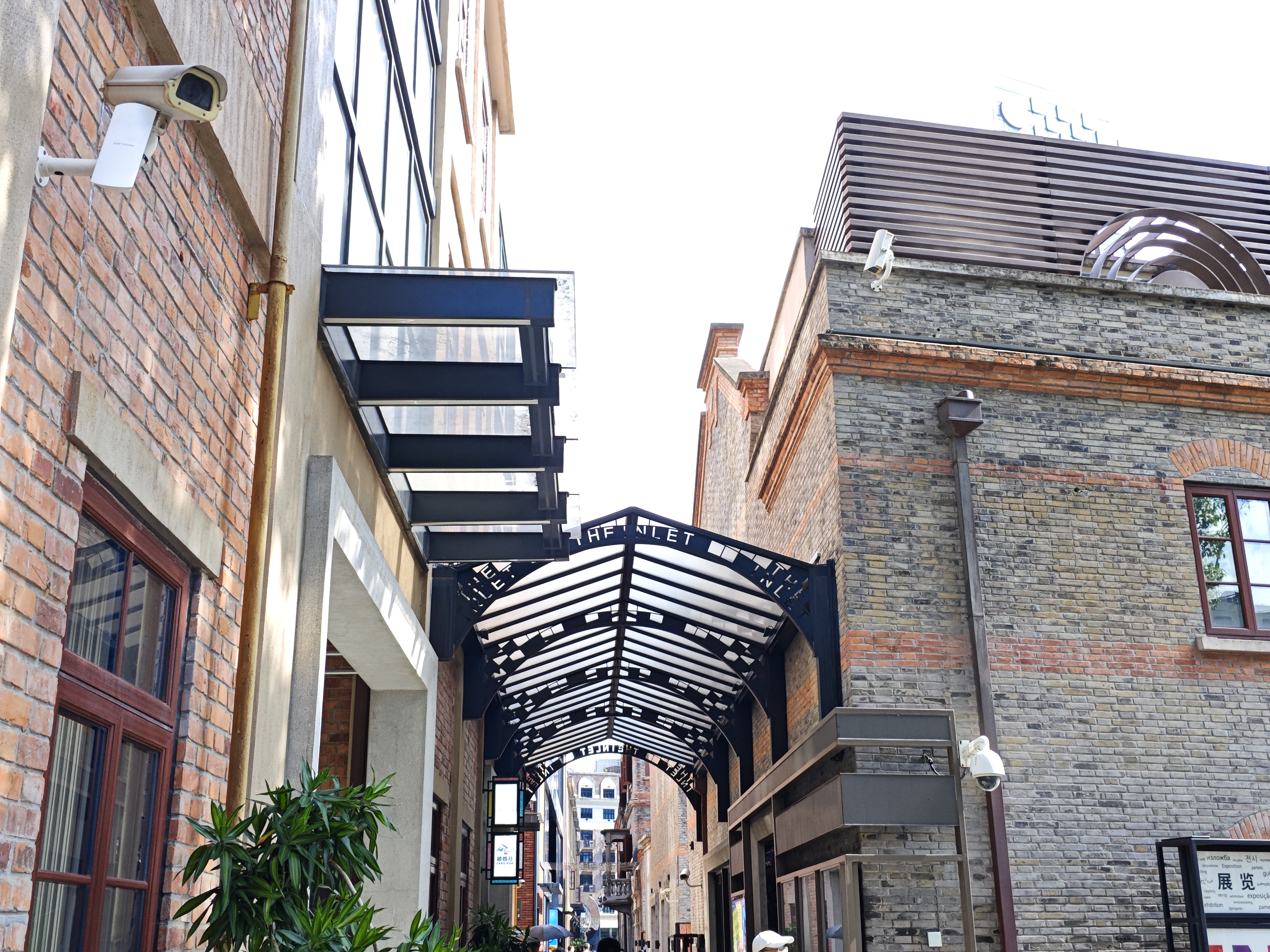Black steel and glass canopy over a brick walkway between buildings